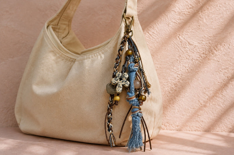 Blue mixed-media tassel bag charm attached to an almond-cream shoulder bag